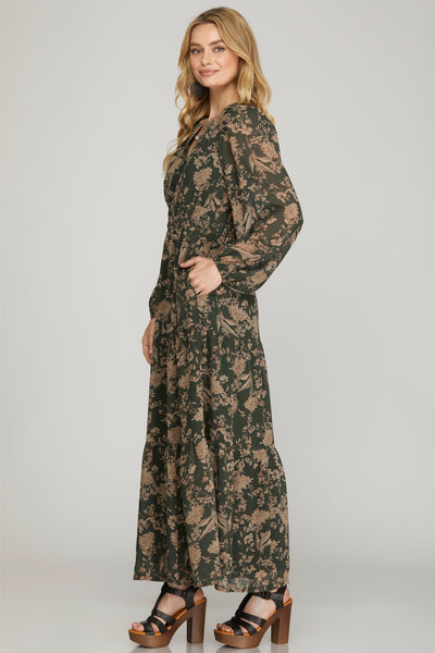Woman wearing a long earthy green floral maxi dress with pockets on a plain background