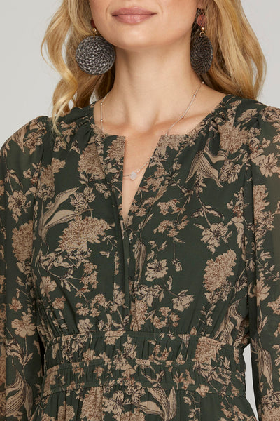 Woman wearing a long earthy green floral maxi dress with pockets on a plain background