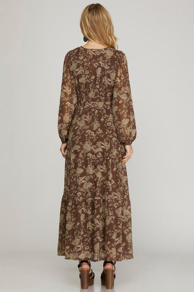 Woman wearing a long earthy brown floral maxi dress with pockets on a plain background