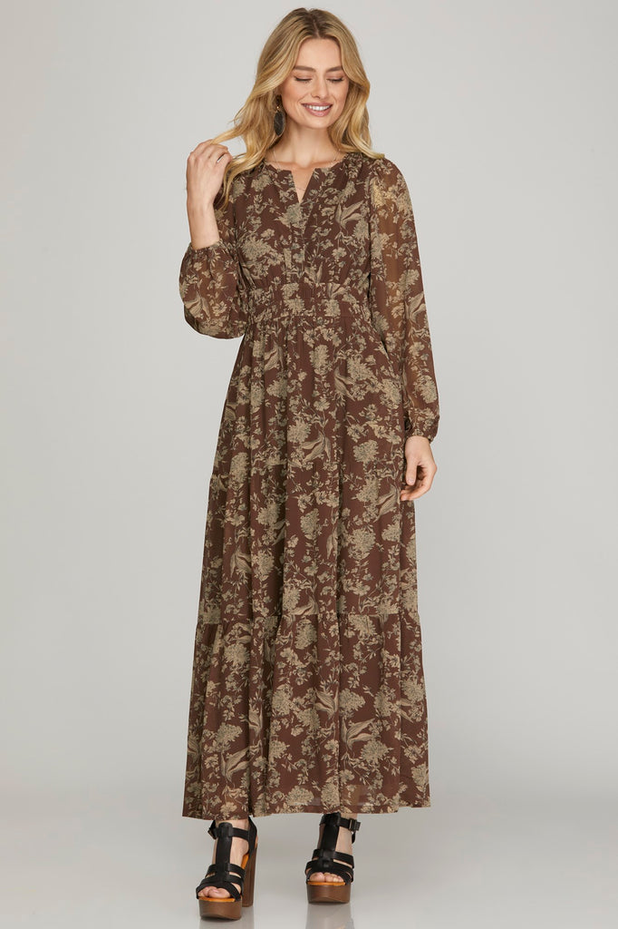 Woman wearing a long earthy brown floral maxi dress with pockets on a plain background