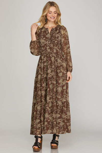 Woman wearing a long earthy brown floral maxi dress with pockets on a plain background