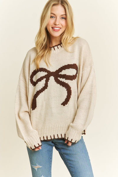 Woman wearing a beige sweater with a large brown bow design on a plain background