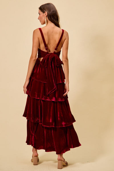 Woman wearing a burgundy velvet dress with a tiered skirt on a beige background