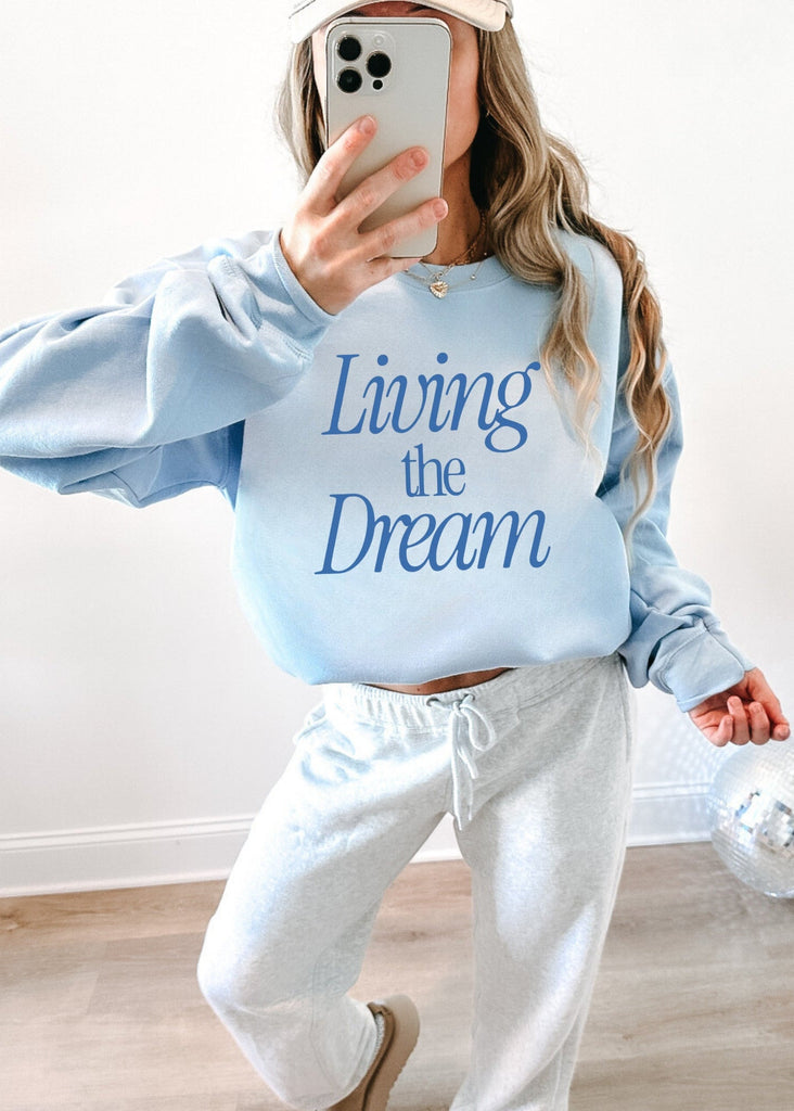 Person wearing a light blue sweatshirt with 'Living the Dream' text, taking a mirror selfie.
