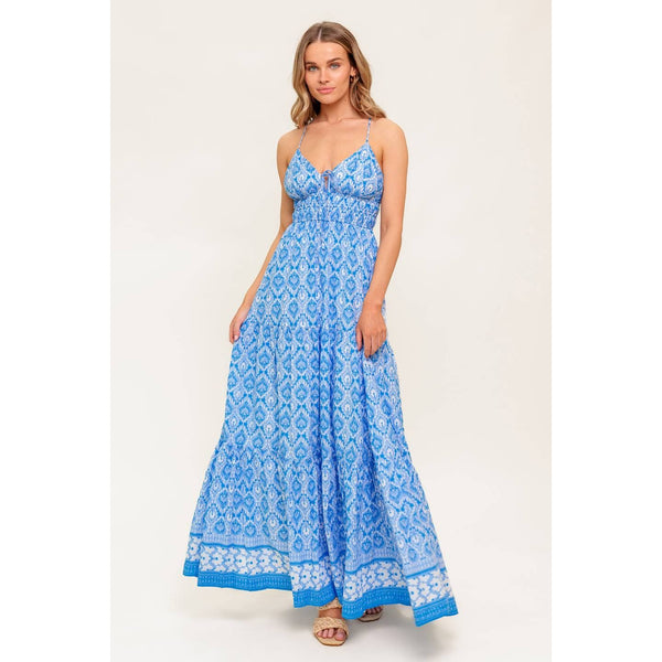 Woman wearing a blue patterned spaghetti-strap maxi dress, with a tie at the chest and a white and blue trim