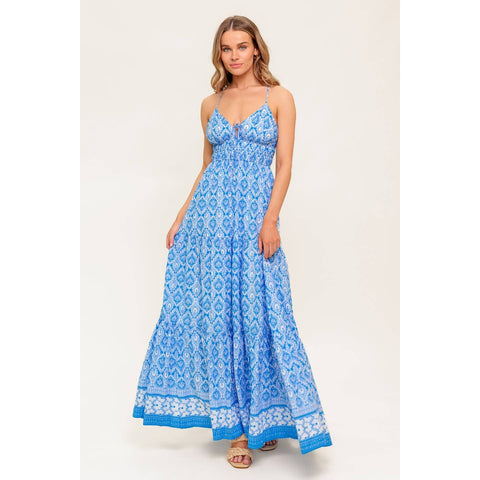 Woman wearing a blue patterned spaghetti-strap maxi dress, with a tie at the chest and a white and blue trim