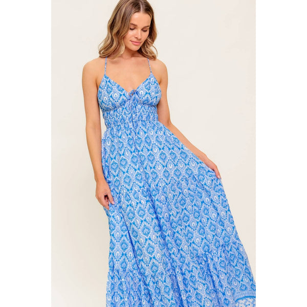 Woman wearing a blue patterned spaghetti-strap maxi dress, with a tie at the chest and a white and blue trim