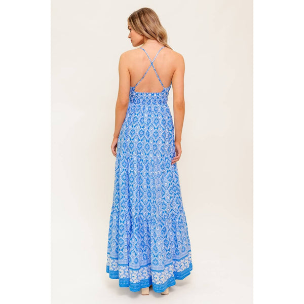 Woman wearing a blue patterned spaghetti-strap maxi dress, with a cross-over back, and a white and blue trim
