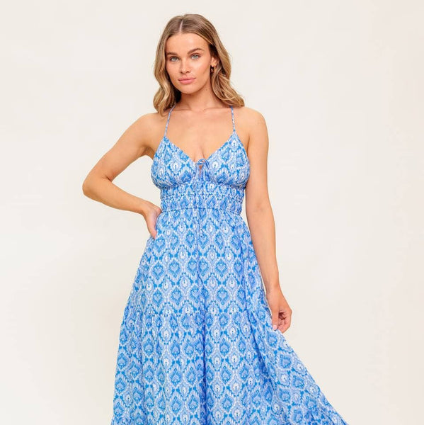 Woman wearing a blue patterned spaghetti-strap maxi dress, with a tie at the chest and a white and blue trim