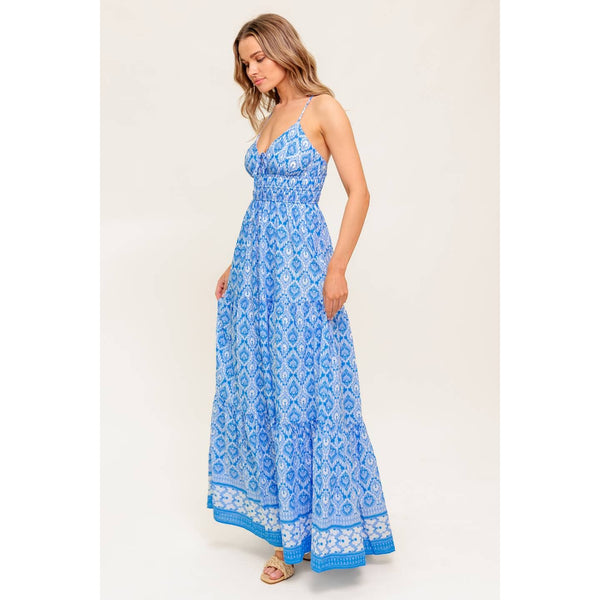 Woman wearing a blue patterned spaghetti-strap maxi dress, with a tie at the chest and a white and blue trim