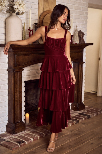 Woman in a burgundy velvet dress standing in a room with a fireplace.