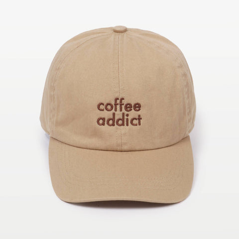 Sandy beige baseball cap with 'coffee addict' embroidered in brown on the front, against a plain background