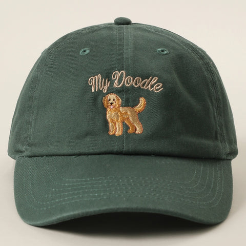 A dark green cotton baseball cap with an embroidered design on the front with the words 'My Doodle' in a light tan script above a matching tan doodle dog illustration