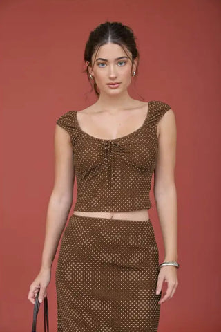 Woman wearing a brown and white polka dot blouse consisting of a scoop-neck crop top with a front tie detail paired with a matching high-waisted pencil skirt, set against a solid terracotta background