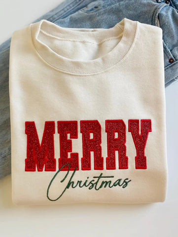 A cream-colored crewneck sweatshirt featuring 'MERRY Christmas' printed on the front, with 'MERRY' in glittery red block letters and 'Christmas' in dark green cursive script