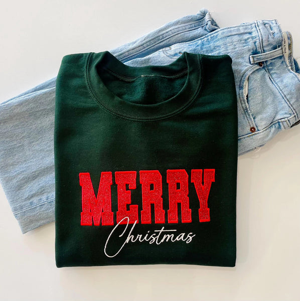 A dark green-colored crewneck sweatshirt featuring 'MERRY Christmas' printed on the front, with 'MERRY' in glittery red block letters and 'Christmas' in white cursive script
