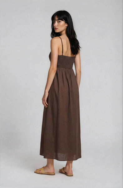 Woman wearing a brown, midi, spaghetti-strap dress against a plain background