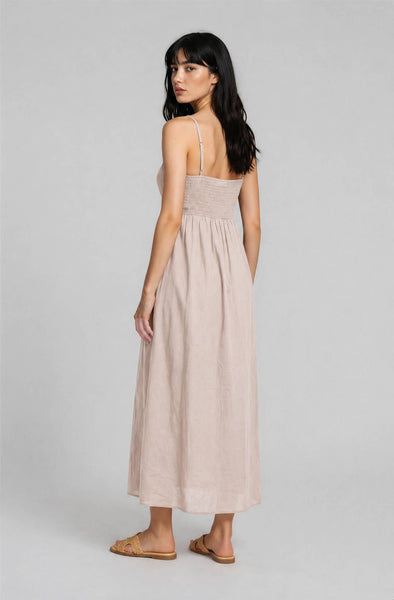 Woman wearing a beige, midi, spaghetti-strap dress against a plain background