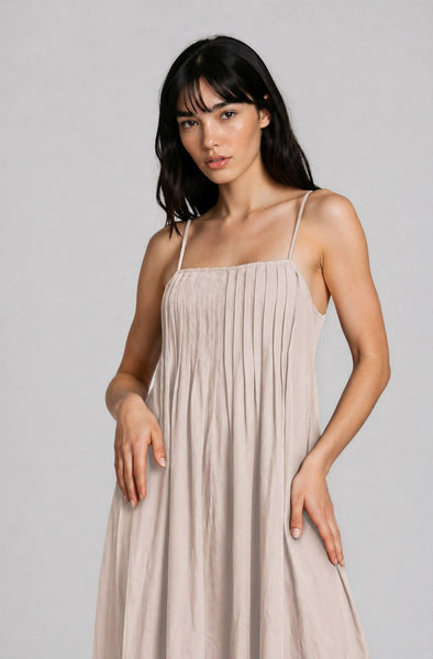 Woman wearing a beige, midi, spaghetti-strap dress against a plain background