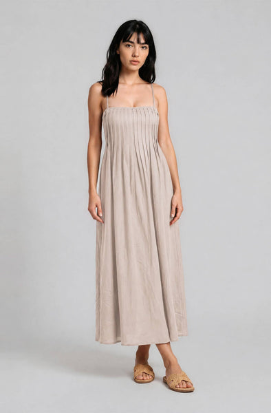Woman wearing a beige, midi, spaghetti-strap dress against a plain background