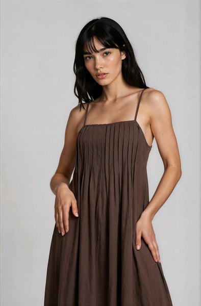 Woman wearing a brown, midi, spaghetti-strap dress against a plain background
