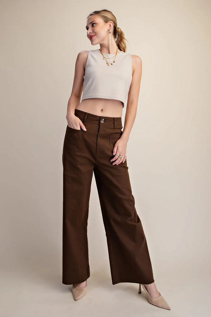 Woman wearing a sleeveless light beige crop top and dark brown wide-leg pants against a plain background