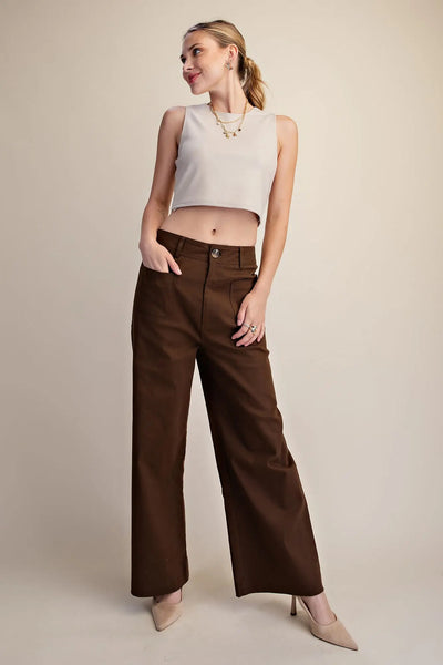 Woman wearing a sleeveless light beige crop top and dark brown wide-leg pants against a plain background