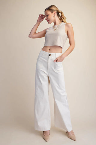 Woman wearing a sleeveless beige crop top and white wide-leg pants against a plain background