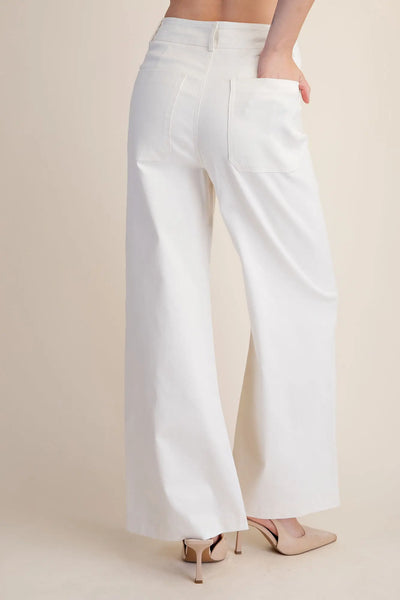 Woman wearing white wide-leg pants against a plain background