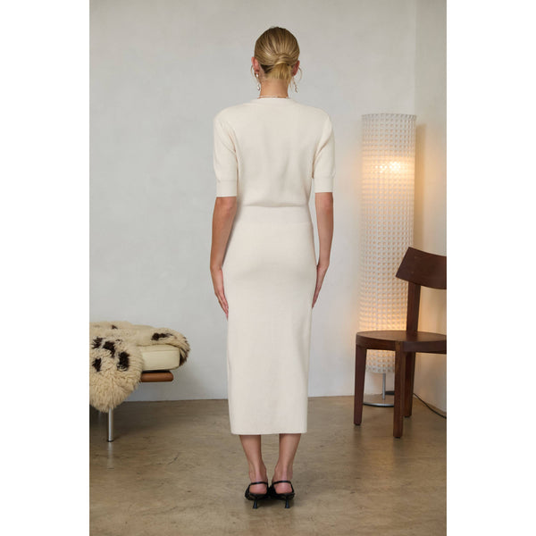 Woman wearing a cream-colored midi dress with short puff sleeves, a V-neckline, and a front button placket with gold buttons, standing indoors.