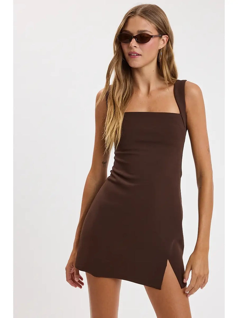 A woman modeling a sleeveless brown mini dress with a square neckline and a side slit, paired with dark sunglasses, against a plain light gray background.