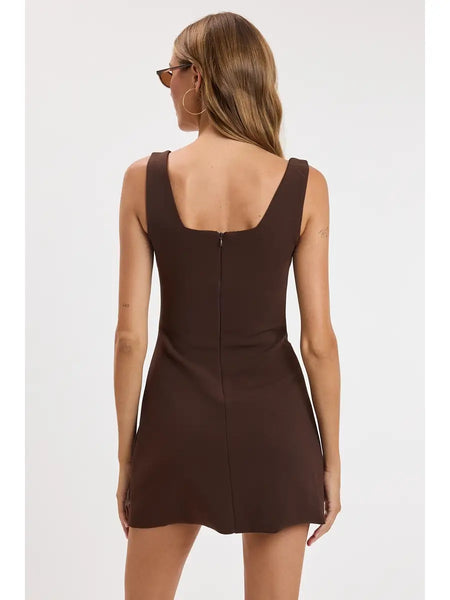 A woman modeling a sleeveless brown mini dress with a square neckline and a side slit, paired with dark sunglasses, against a plain light gray background.
