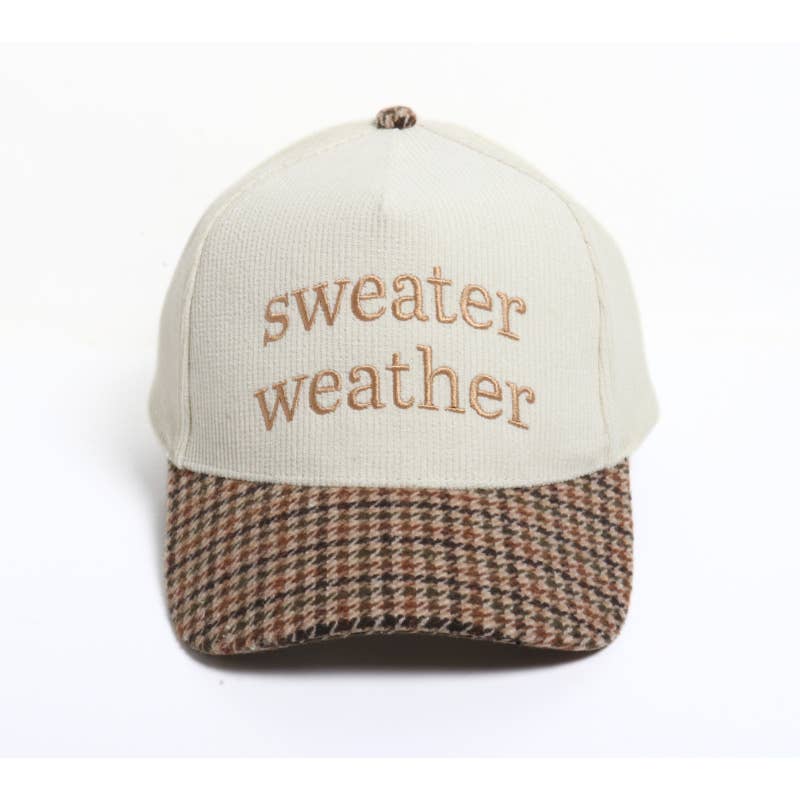 A baseball cap with an off-white crown and a brown, beige, and black houndstooth patterned visor. The front of the cap features the embroidered text 'sweater weather' in a tan text